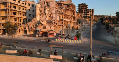 People sit in front of Abu Ali's cafe, set up on the ground floor of a building heavily damaged during the civil war, in the of Ariha in the opposition-held northwestern Idlib province, Syria, July 11, 2021. (Photo by Aaref Watad/AFP)