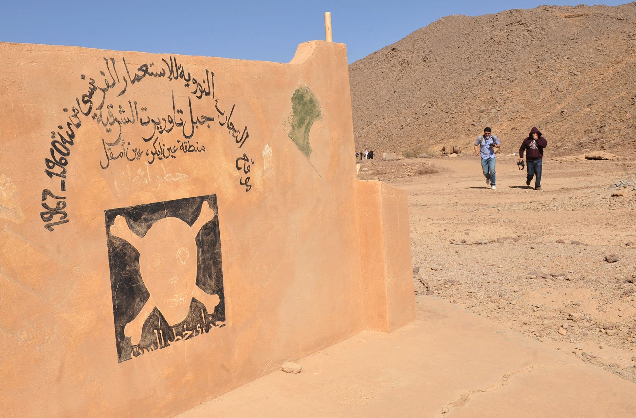 Two people walk near a danger of death sign at the entrance of the former French nuclear bomb test site of Tena Fila mountain at Ain Ekra in Tamanrasset, 2,000 kilometers (1,242 miles) south of Algiers, Algeria, Feb. 25, 2010. (AFP Photo)