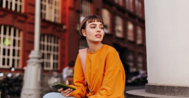 Cheerful young girl in an orange sweatshirt and jeans walks outdoors. (Shutterstock Photo) 