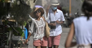Tourists walk through water sprayed by a mister at a cafe during a heatwave in Athens, Greece, July 29, 2021. (AFP Photo)