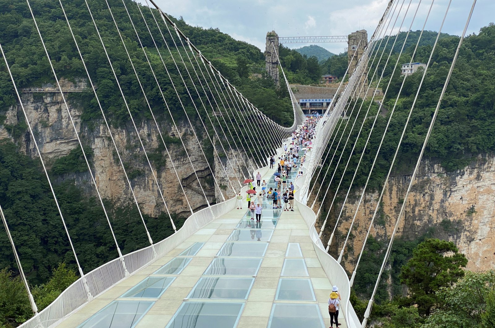 Visitors walk on a 430-meter (1,410-foot) long glass-bottomed bridge over the Zhangjiajie Grand Canyon in Zhangjiajie, Hunan province, China, July 8, 2021. (Reuters Photo)