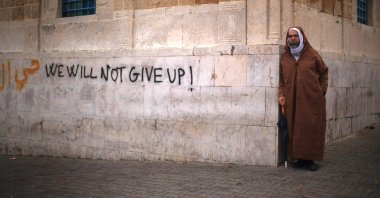 A Tunisian man looks on next to graffiti as protestors continue their demonstrations outside then-Prime Minister Mohammed Ghannouchi's offices in Tunis, Tunisia, Jan. 25, 2011. (Photo by Getty Images)