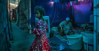 A young Rohingya refugee girl walks past an elderly man sitting inside a tent at a refugee camp alongside the banks of the Yamuna River on the southeastern border of New Delhi, India, July 1, 2021. (AP Photo)