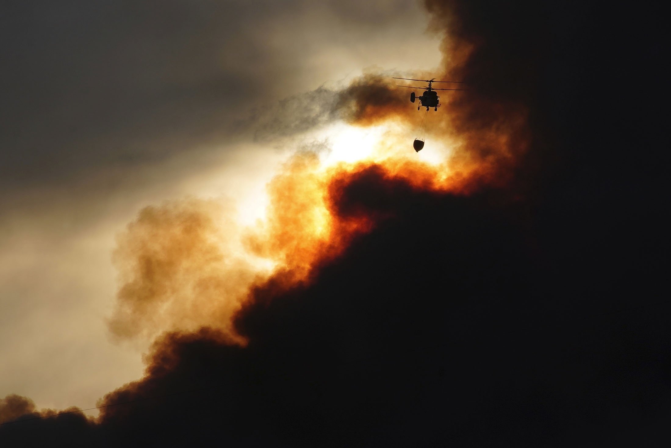 A firefighting helicopter carries water to drop on a wildfire in Santa Coloma de Queralt, near Tarragona, Spain, July 25, 2021. (AP Photo)