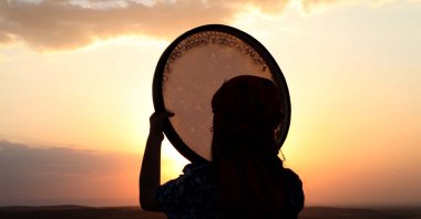 A woman holds a daf, a Middle Eastern frame drum musical instrument, as the sun sets upon the Zerzevan Castle, Diyarbakır, Turkey, July 31, 2021. (AA Photo)