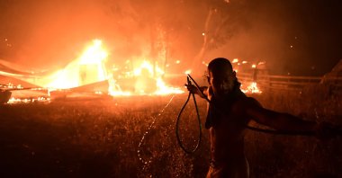 A man uses a water hose during a wildfire in Adames area, in northern Athens, Greece, Aug. 3, 2021. (AP Photo)