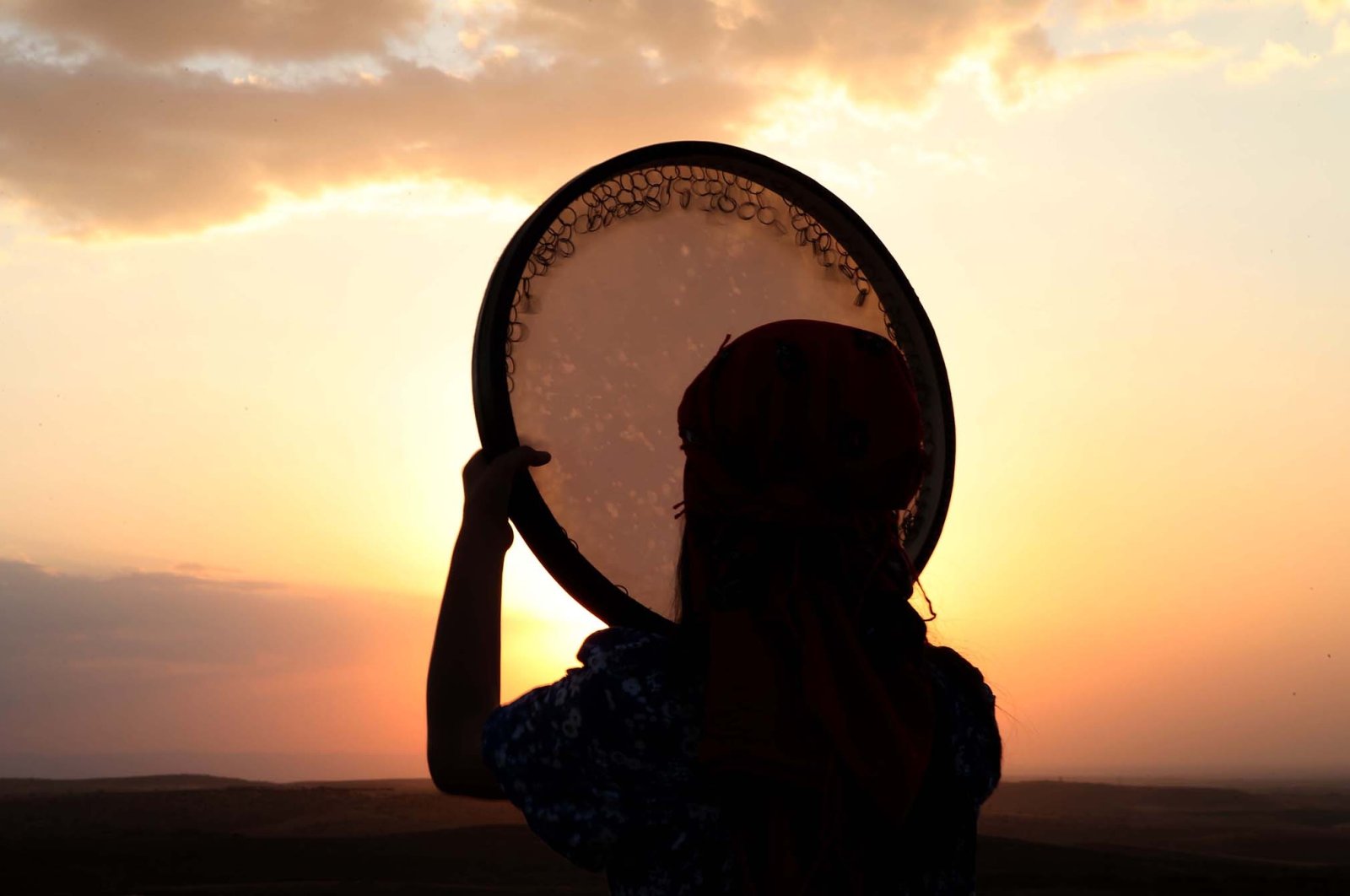 A woman holds a daf, a Middle Eastern frame drum musical instrument, as the sun sets upon the Zerzevan Castle, Diyarbakır, Turkey, July 31, 2021. (AA Photo)