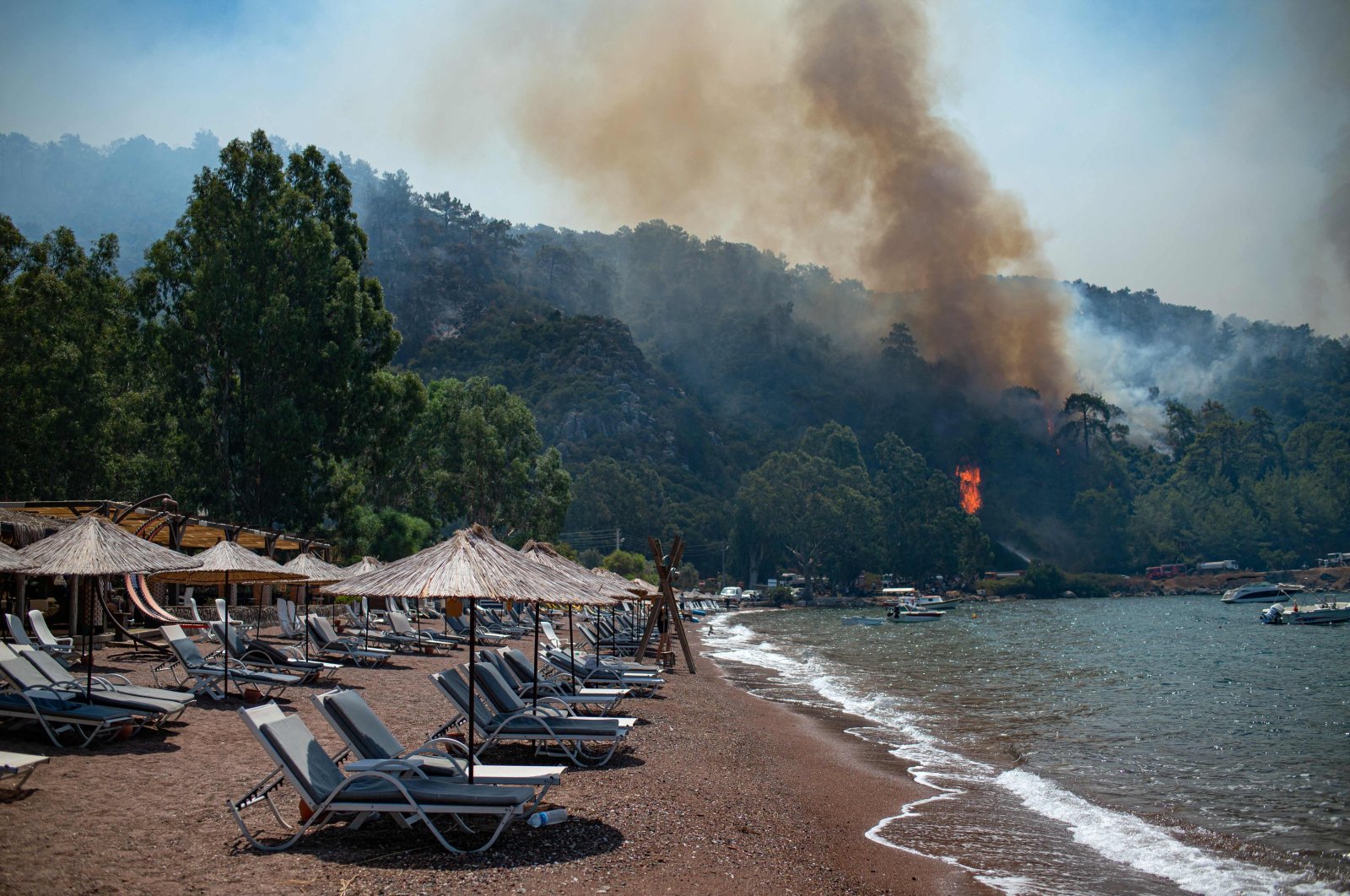 Deck chairs are seen on a beach in front of smoke and flames rising from a forest fire in the Muğla district of Marmaris, Turkey, Aug. 3, 2021. (AFP Photo)