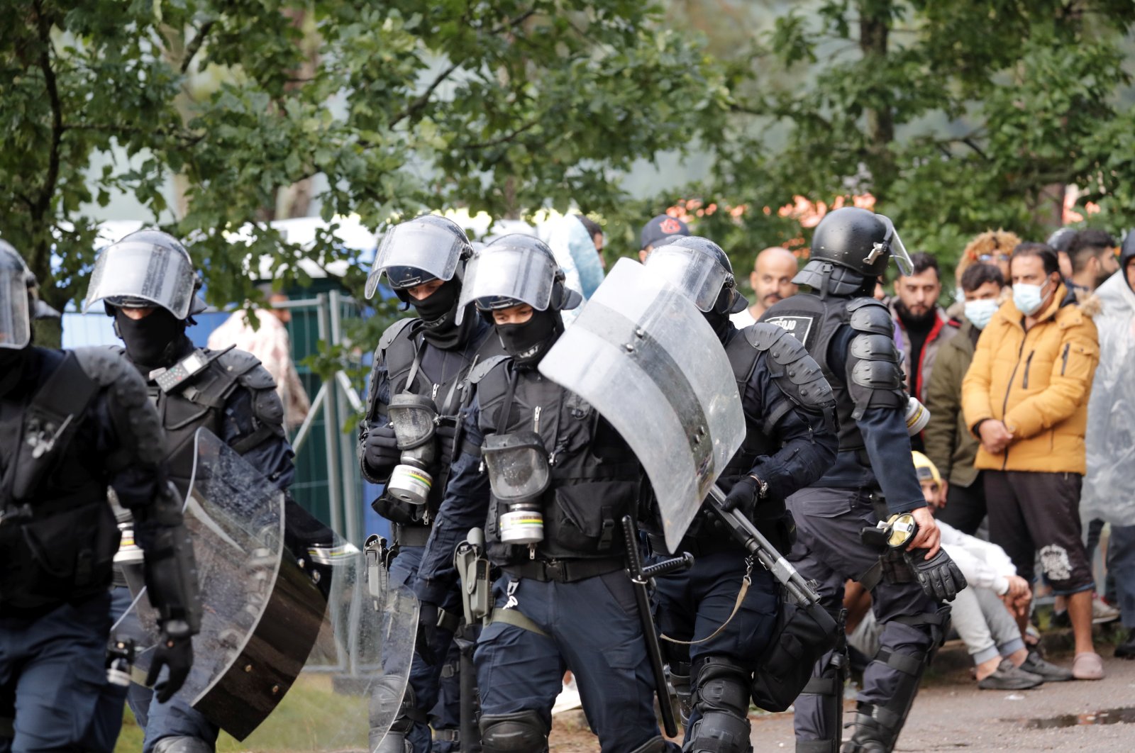 Riot police officers and migrants are seen at the tent camp in the Rudninkai training ground, Lithuania, Aug. 2, 2021. (EPA Photo)