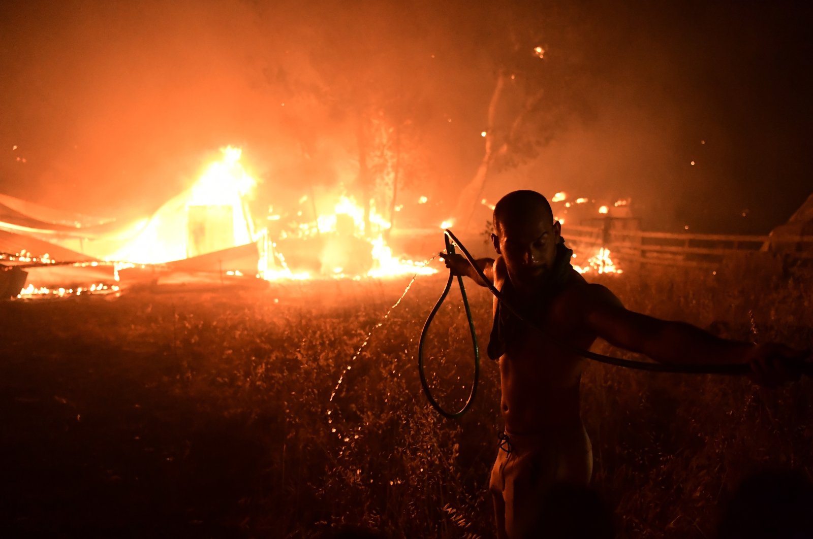 A man uses a water hose during a wildfire in Adames area, in northern Athens, Greece, Aug. 3, 2021. (AP Photo)