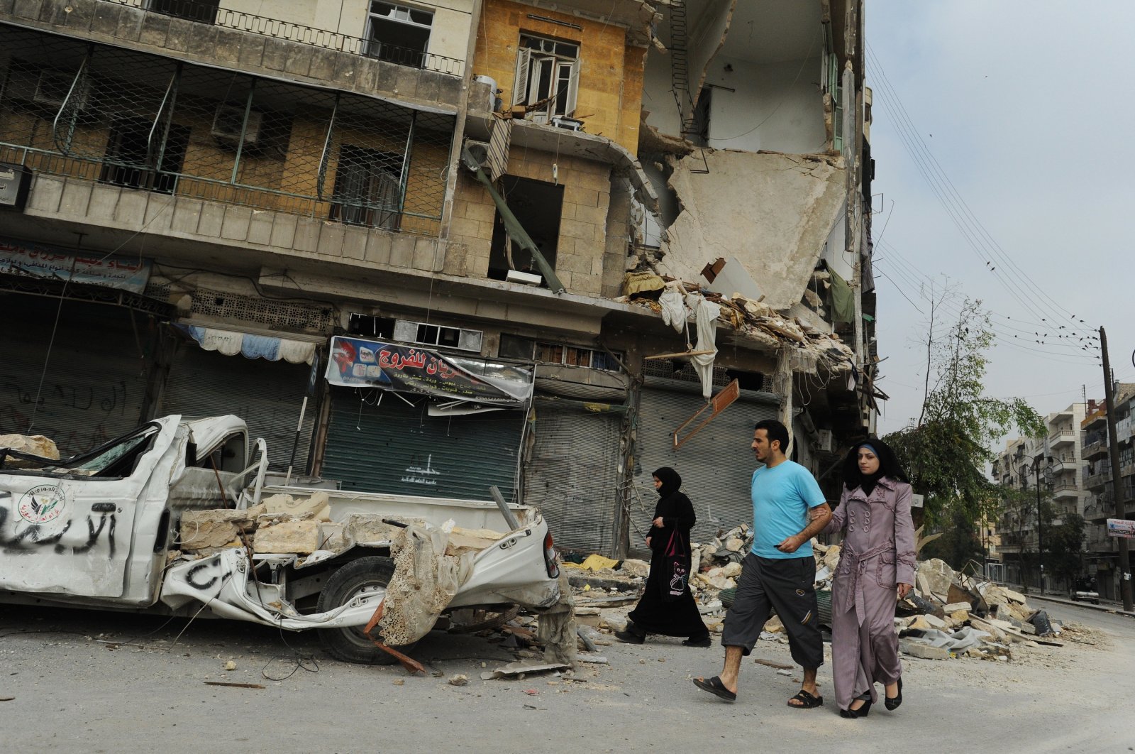 Syrians walk past a destroyed vehicle as they come to terms with massive destruction from regime air and artillery bombardment in Aleppo, Syria, Oct. 23, 2012. (Getty Images)