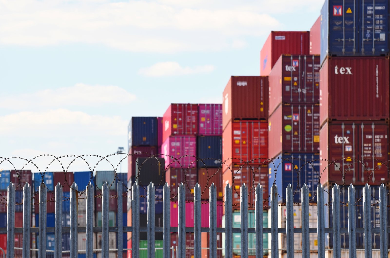Freight shipping containers piled up high behind a fence topped with barbed wire in one of the U.K.'s busiest ports, Southampton, U.K., May 31, 2020. (Shutterstock Photo)