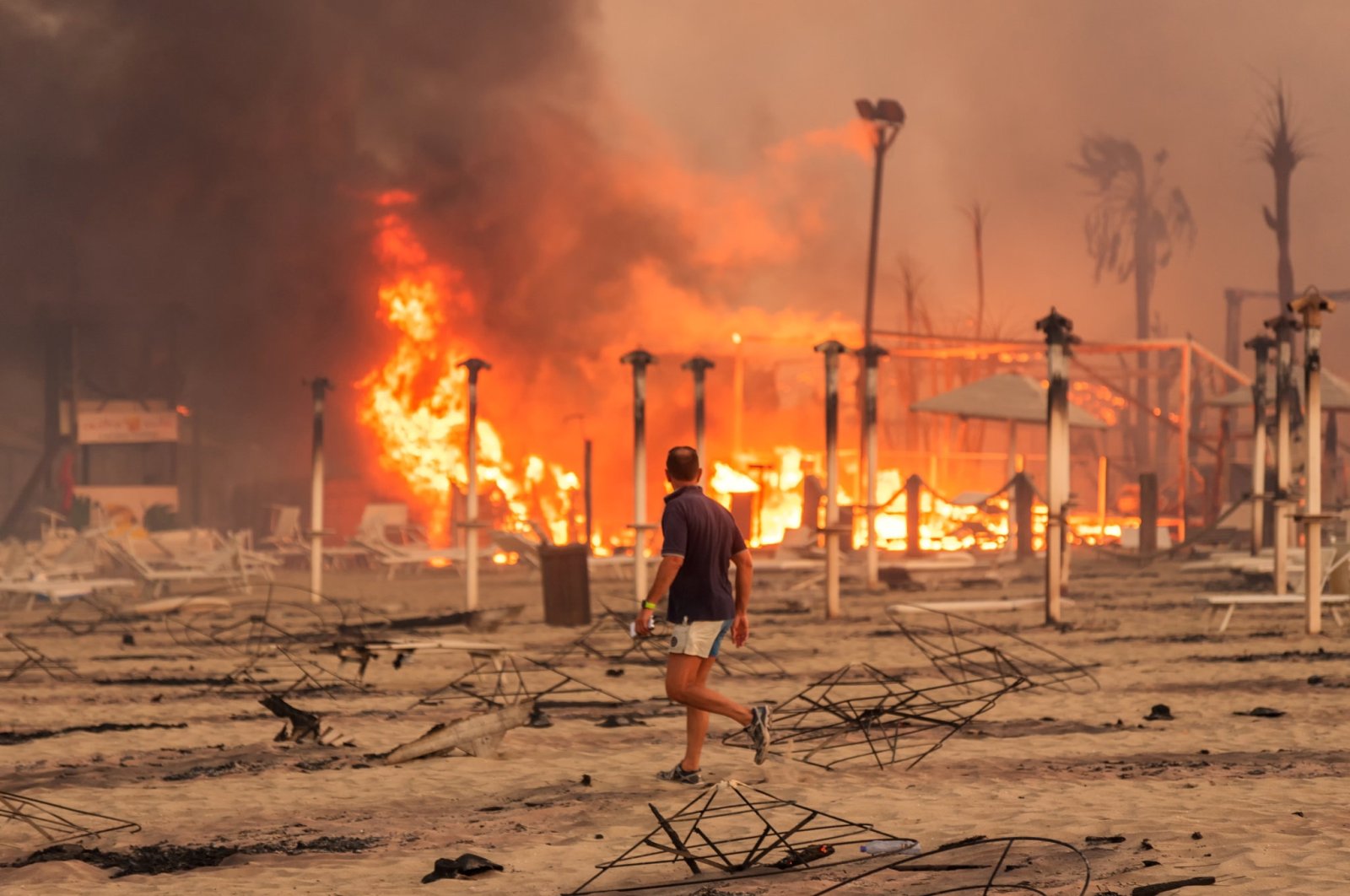 A man walks in front of a fire at Le Capannine beach in Catania, Sicily, Italy, July 30, 2021.  (Roberto Viglianisi via Reuters)