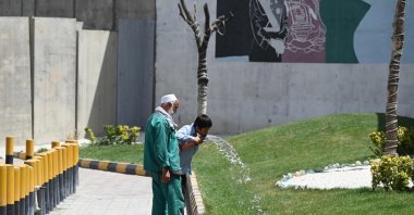 A schoolboy drinks water from a pipe as a gardener looks on, Kabul, Afghanistan, Aug. 5, 2021. (AFP Photo)