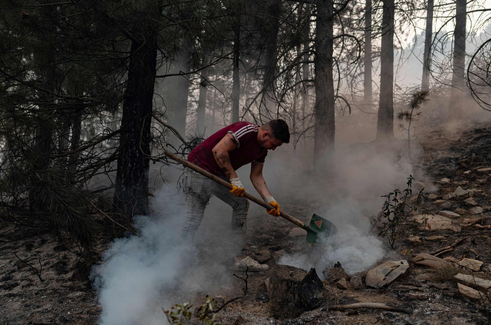 A volunteer from a nearby village uses a shovel to help contain smouldering forest fires in the hills of a recently burnt area near Kavaklıdere, a town in Muğla province, Turkey, Aug. 5, 2021. (AFP Photo)