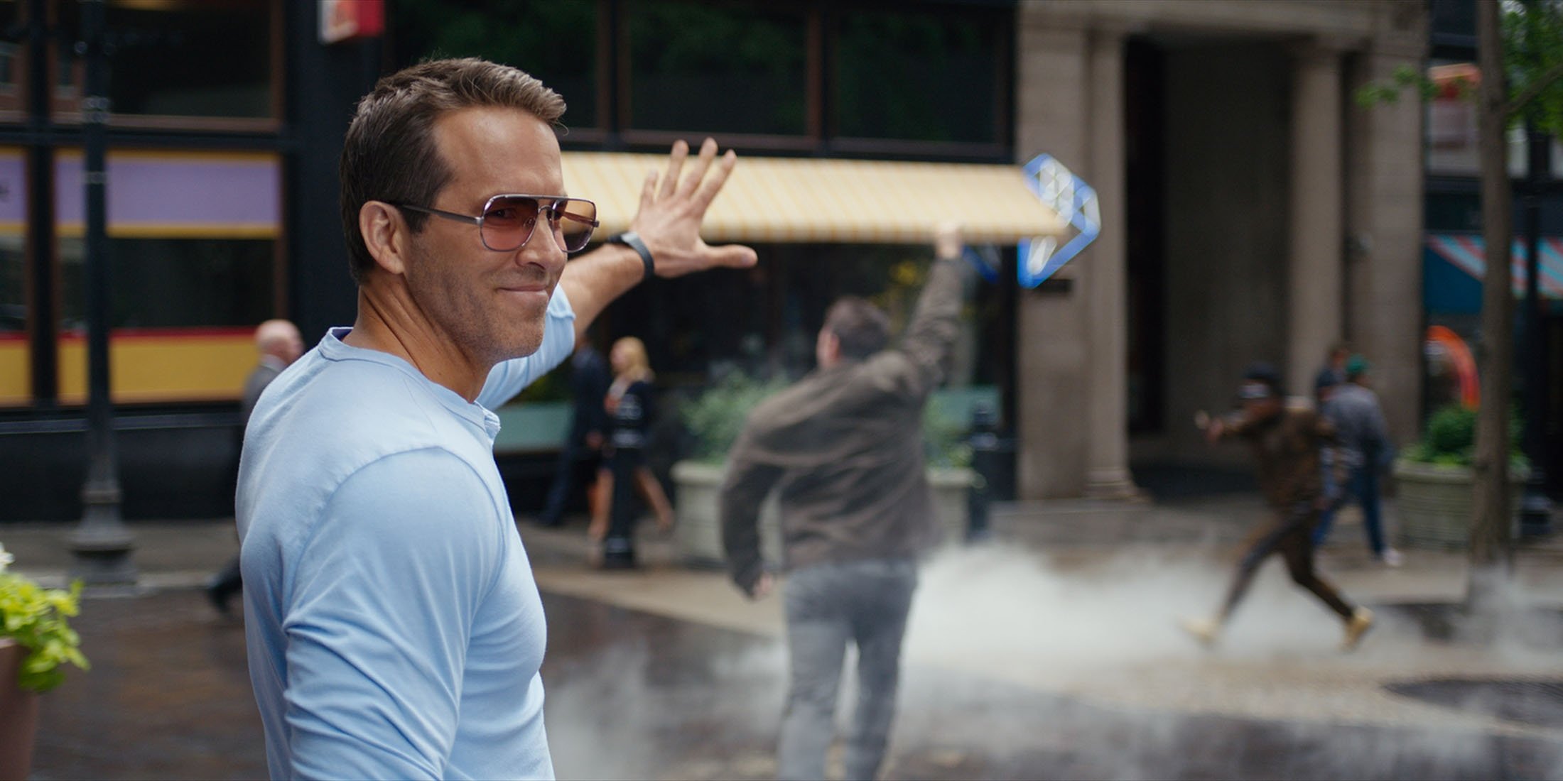 Ryan Reynolds waves as he smiles at a scene in the movie 