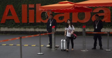 A woman pushing a trolley bag passes by security guards at the entrance to the Alibaba Group headquarters in Hangzhou, in Zhejiang province, eastern China, May 27, 2016. (AP Photo)