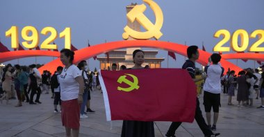 A woman holds up a Communist Party flag as she poses for photos near decorations to mark the 100th anniversary of the founding of the ruling Chinese Communist Party on Tiananmen Square in Beijing, China, on July 15, 2021. (AP Photo)