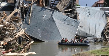 Military personnel floats on a boat on the Ahr river as the roof of a damaged house hangs on the water in Rech, Rhineland-Palatinate, after devastating floods hit the region, western Germany, July 21, 2021. (AFP Photo)
