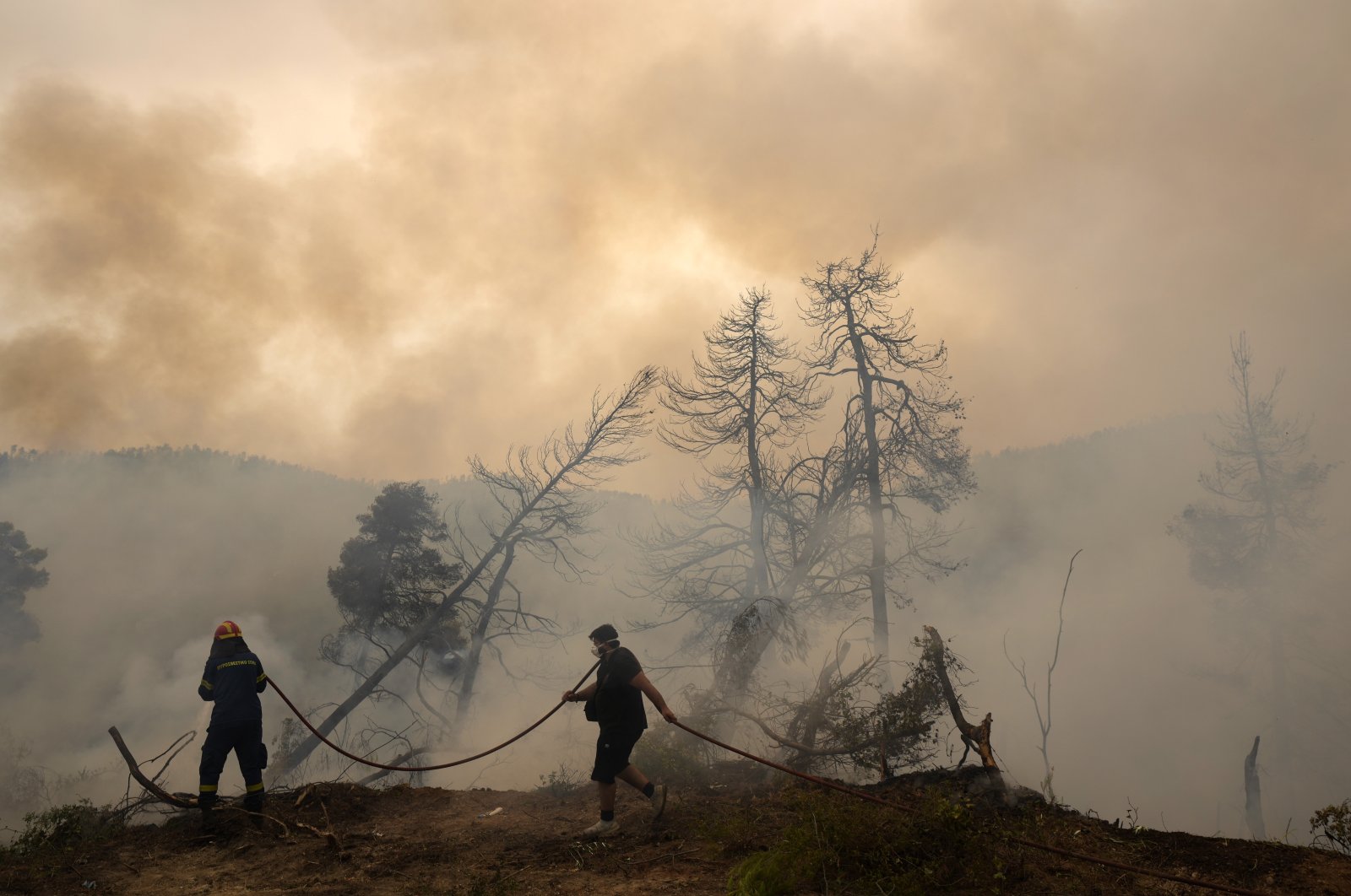 A firefighter tries to extinguish the flames as a local resident holds a water hose during a wildfire at Ellinika village on Evia island, about 176 kilometers (110 miles) north of Athens, Greece, Aug. 9, 2021. (AP Photo)