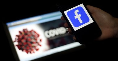 The Facebook logo is displayed on a mobile phone screen photographed on a COVID-19 illustration graphic background in Arlington, Virginia, March 25, 2020. (AFP Photo)