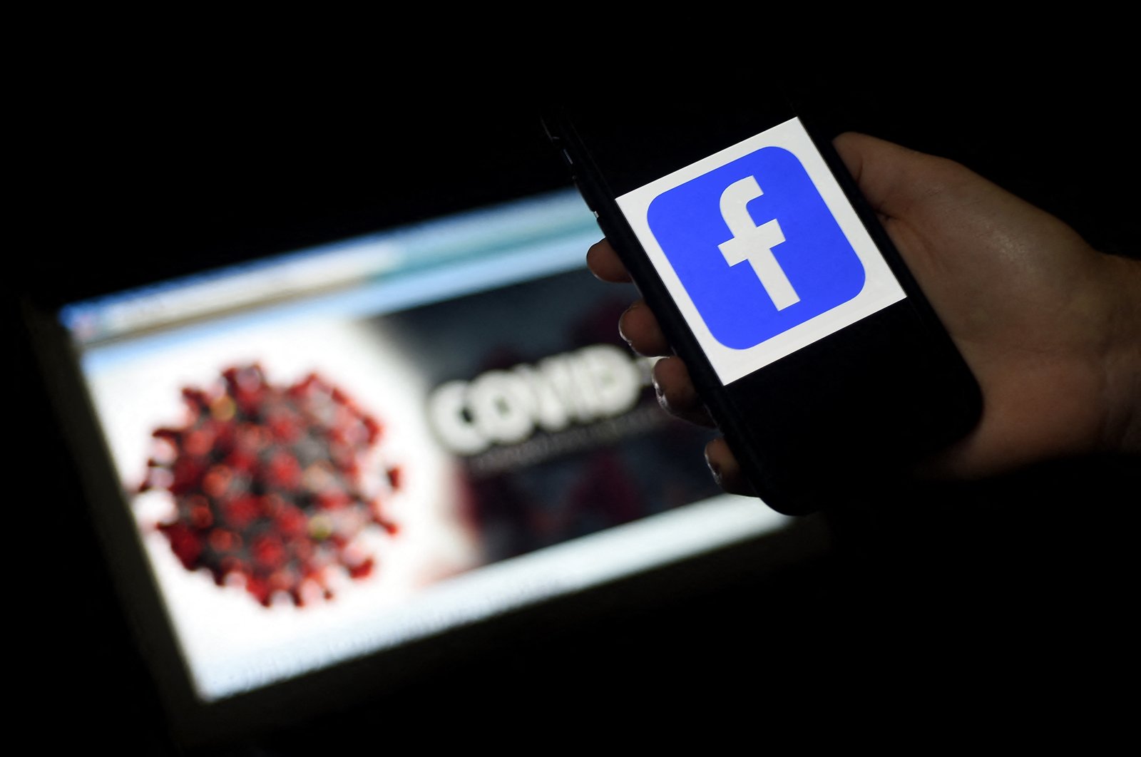 The Facebook logo is displayed on a mobile phone screen photographed on a COVID-19 illustration graphic background in Arlington, Virginia, March 25, 2020. (AFP Photo)