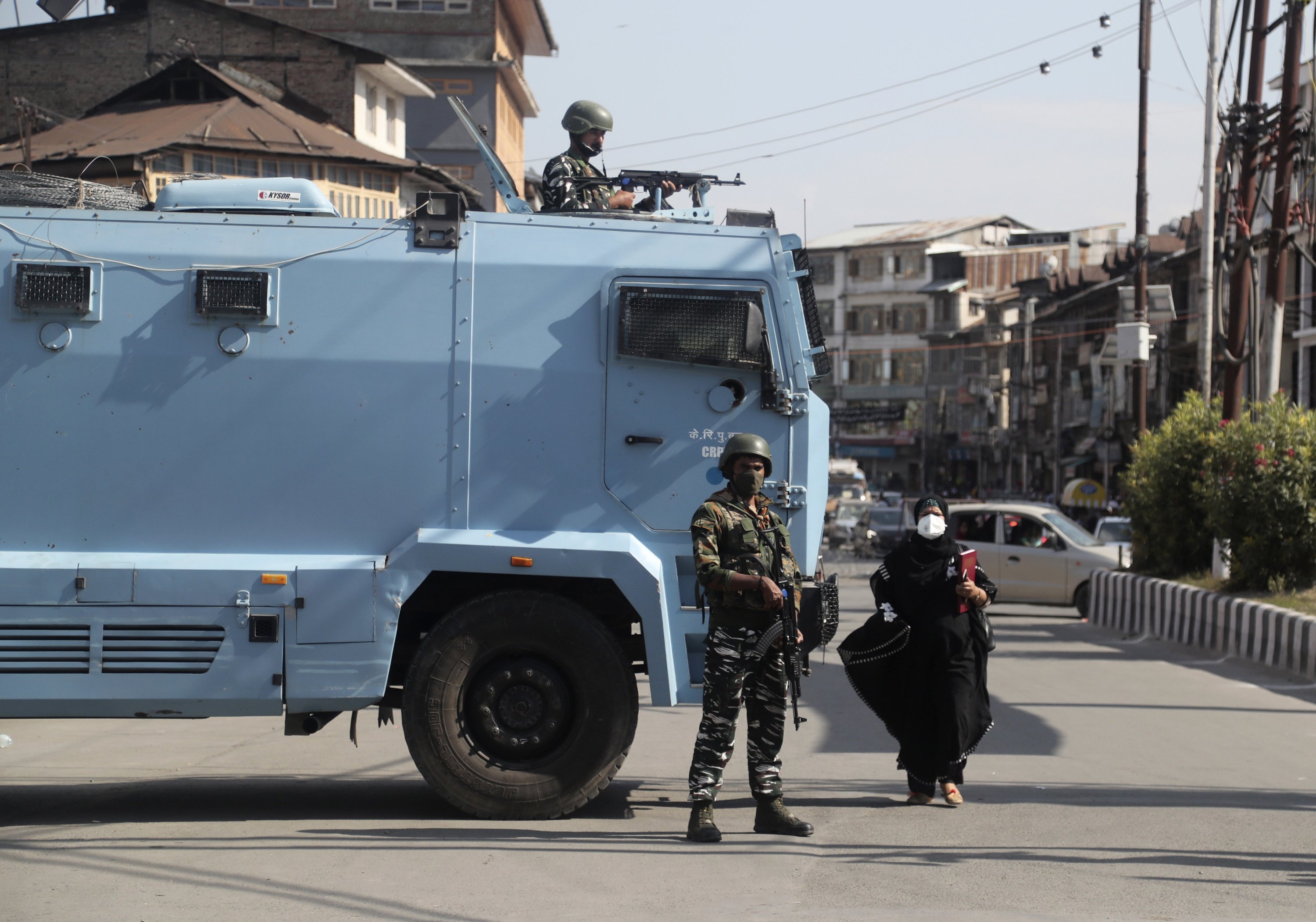 A Kashmiri woman walks past Indian paramilitary soldiers standing guard near the site of a grenade attack at a busy market in Srinagar, Indian controlled Kashmir, Tuesday, Aug. 10, 2021. (AP Photo)