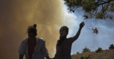 People watch as a helicopter participates in a wildfire extinguishing operation, in Köyceğiz, Muğla, southwestern Turkey on Aug. 9, 2021. (AP Photo)