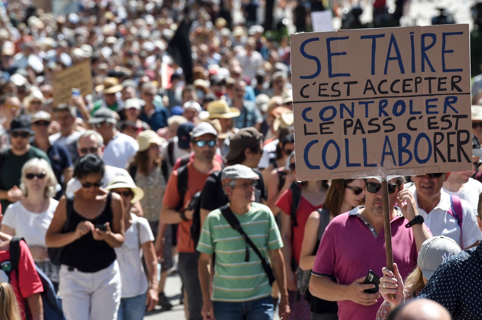 A protester holds a placard reading "To keep silent is to accept. To control is to collaborate" during a national day of protest against the compulsory COVID-19 vaccination for certain workers, and the mandatory use of the health pass called for by the French government to access most public spaces, in Nantes, Western France, Aug. 14, 2021.   (AFP Photo)