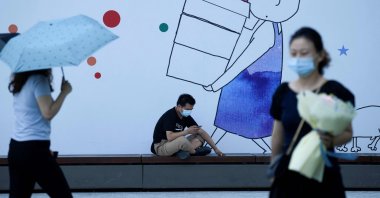 A man wearing a face mask uses his mobile phone in front of an advertisement in Beijing, China, Aug. 11, 2020. (AFP Photo)