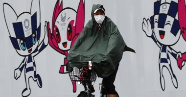 A person wearing a rain coat rides a bicycle in front of a wall decoration featuring Tokyo 2020 Olympic Games mascot Miraitowa and Paralympics mascot Someity, Tokyo, Japan, July 27, 2021. (Reuters Photo)
