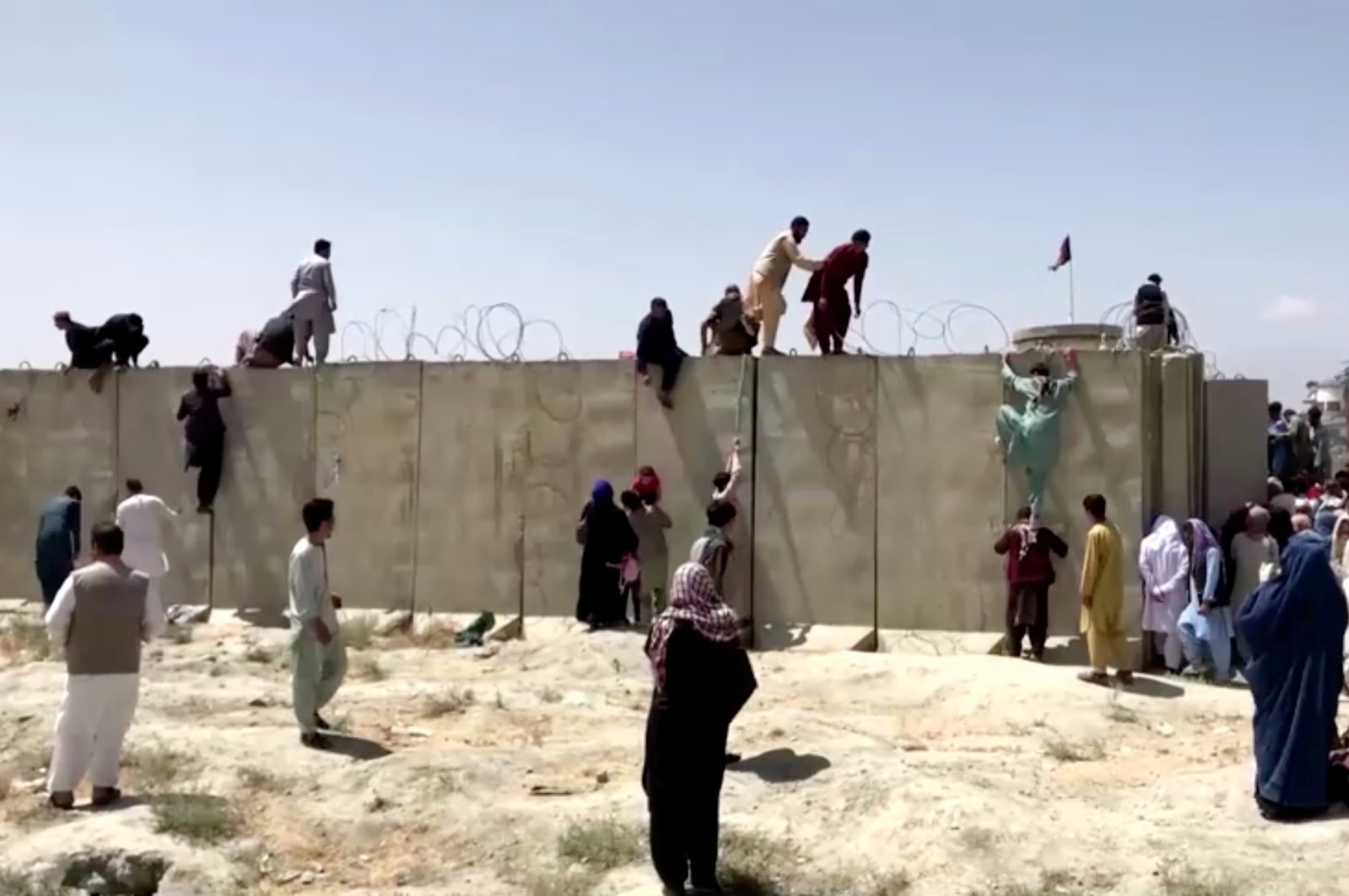 People climb a barbed wire wall to enter the Kabul Hamid Karzai International Airport, Kabul, Afghanistan, Aug. 16, 2021. (REUTERS Photo)