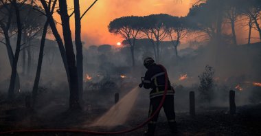 A French firefighter uses a water hose as light from the setting sun is filtered through smoke during a forest wildfire, near Gonfaron, in Var Prefecture, southern France, Aug. 17, 2021. (AFP Photo)
