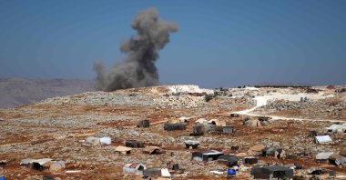 A plume of smoke rises behind a hill, where internally displaced Syrians have set up tents, during reported airstrikes by pro-regime forces, north of the opposition-held city of Idlib, Syria, Aug. 20, 2021. (AFP Photo)