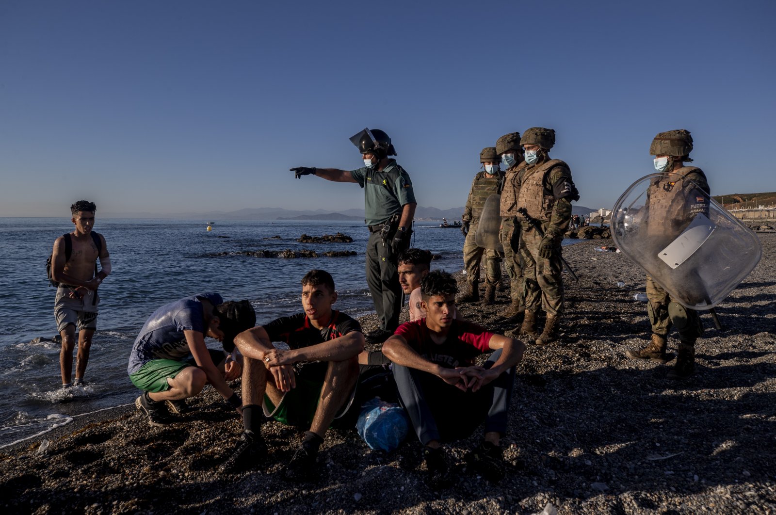 Migrants are surrounded by Spanish security forces on a beach after arriving at the Spanish enclave of Ceuta, near the border of Morocco and Spain, May 19, 2021. (AP Photo)