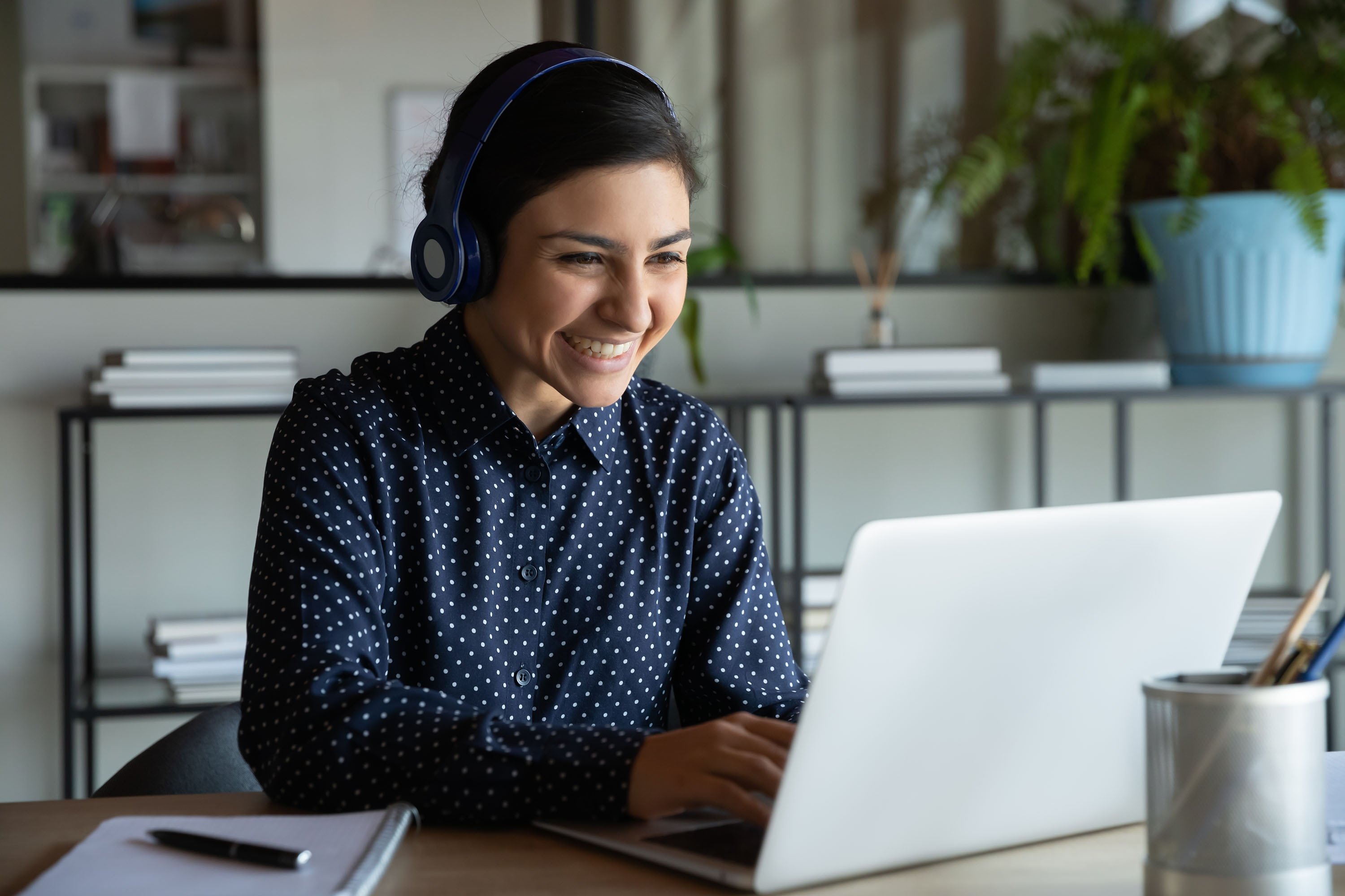 A young professional wearing wireless headphones looks at her laptop screen. (Shutterstock Photo)