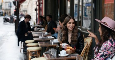 Emily, played by Lily Collins, sits with a friend in a Parisian cafe in the first season of the Netflix series "Emily in Paris." (DPA Photo) 