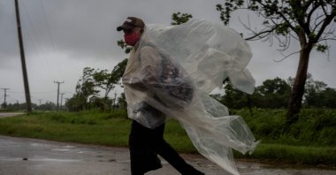 A man, wearing a makeshift poncho to protect himself from the rains of Hurricane Ida, walks on a road leading to Batabano, in the Mayabeque province, Cuba, Aug. 27, 2021. (AP Photo)