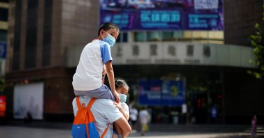 A man carries two children, all wearing protective face masks following new cases of COVID-19, on a street in Shanghai, China, Aug. 25, 2021. (Reuters Photo)