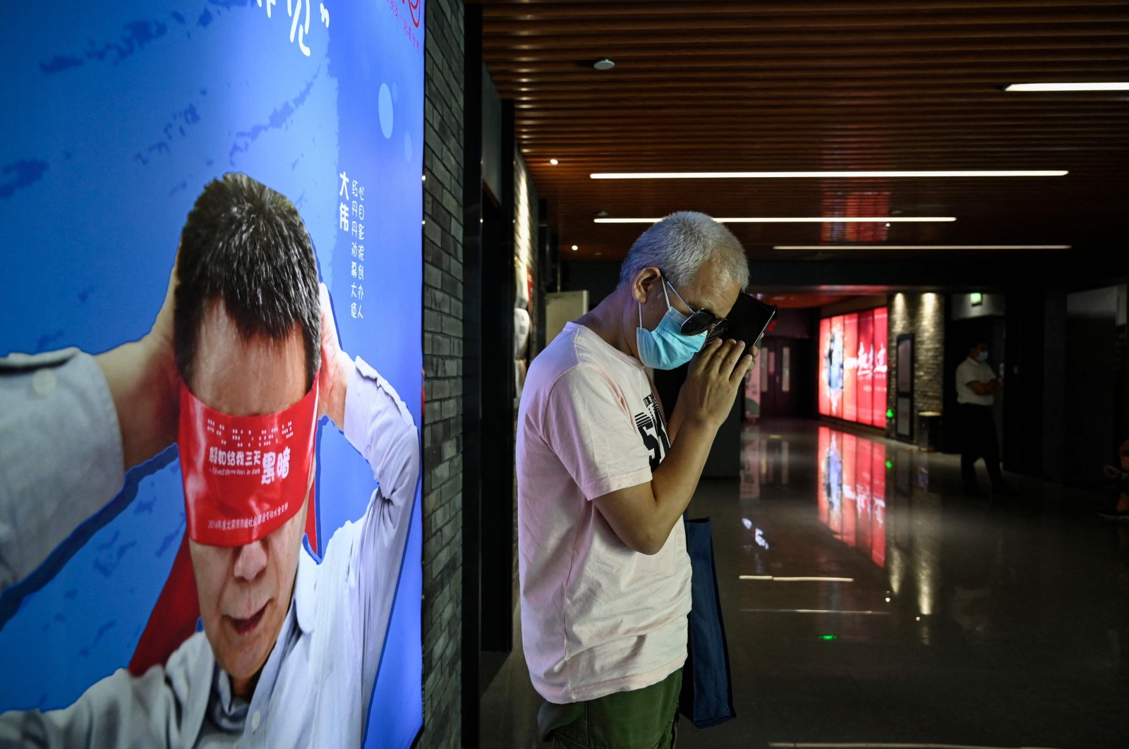 Visually impaired massage therapist Zhang Xinsheng uses his phone in front of a billboard supporting visually impaired people, at a cinema in Beijing, China, Aug. 7, 2021. (AFP Photo)