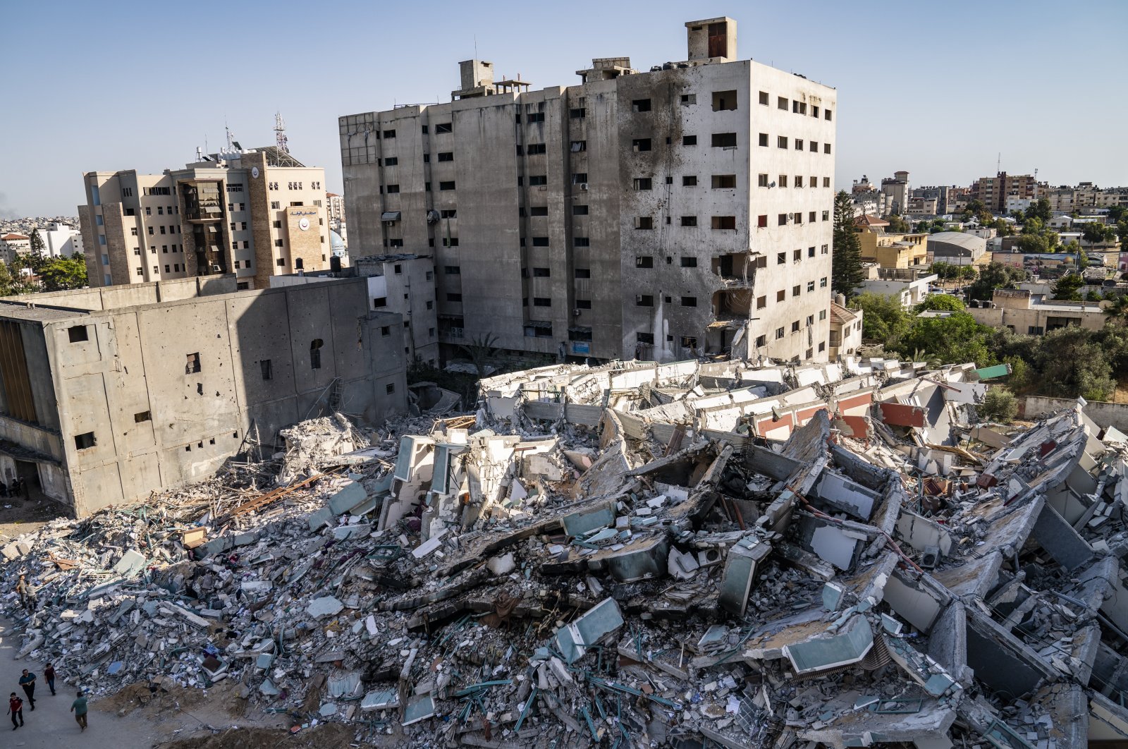 People walk past the rubble of the 12-story al-Jalaa building that was destroyed in an Israeli airstrike, having before been the Associated Press bureau in Gaza City for 15 years and housed dozens of families, in Gaza City, the Gaza Strip, Palestine, May 21, 2021. (AP Photo)
