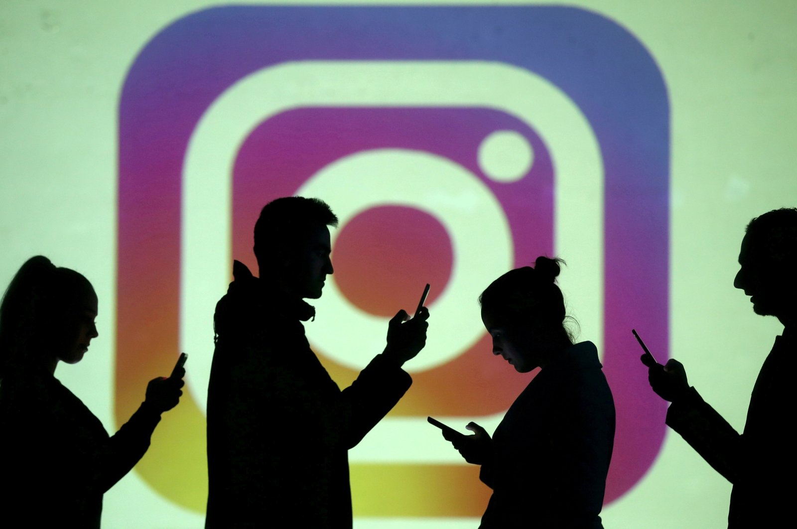 Silhouettes of mobile users are seen next to a screen projection of Instagram logo, March 28, 2018. (REUTERS File Photo)