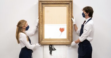 Art handlers at Sotheby's auction house hold Banksy's “Love is in the Bin,” before it returns to auction at Sotheby's, London, U.K., Sept. 3, 2021. (AP Photo)