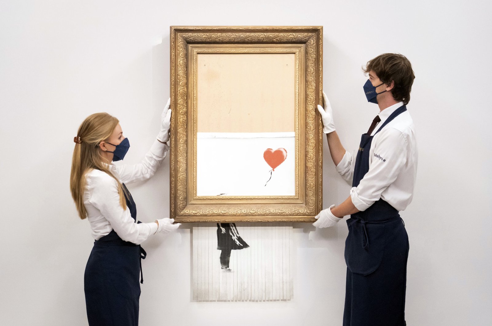 Art handlers at Sotheby's auction house hold Banksy's “Love is in the Bin,” before it returns to auction at Sotheby's, London, U.K., Sept. 3, 2021. (AP Photo)