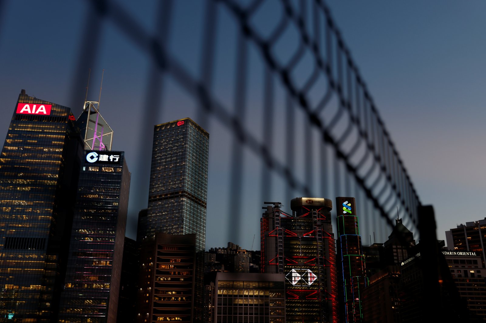 Skyscrapers at the central business district, including AIA Central, China Construction Bank (CCB) Tower, Bank of China Tower, Cheung Kong Centre, HSBC and Standard Chartered Bank headquarters, are seen through a fence during sunset in Hong Kong, Aug. 17, 2021. (Reuters Photo)