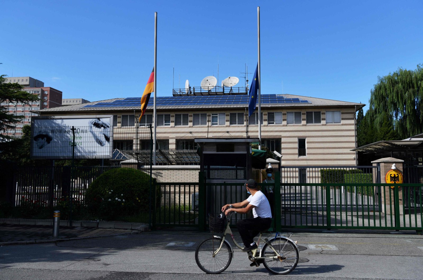 A man cycles past the German and EU flags flying at half-mast at the German Embassy in Beijing on Sept. 6, 2021, after the announcement of the death of Germany's ambassador to China Jan Hecker. (AFP Photo)
