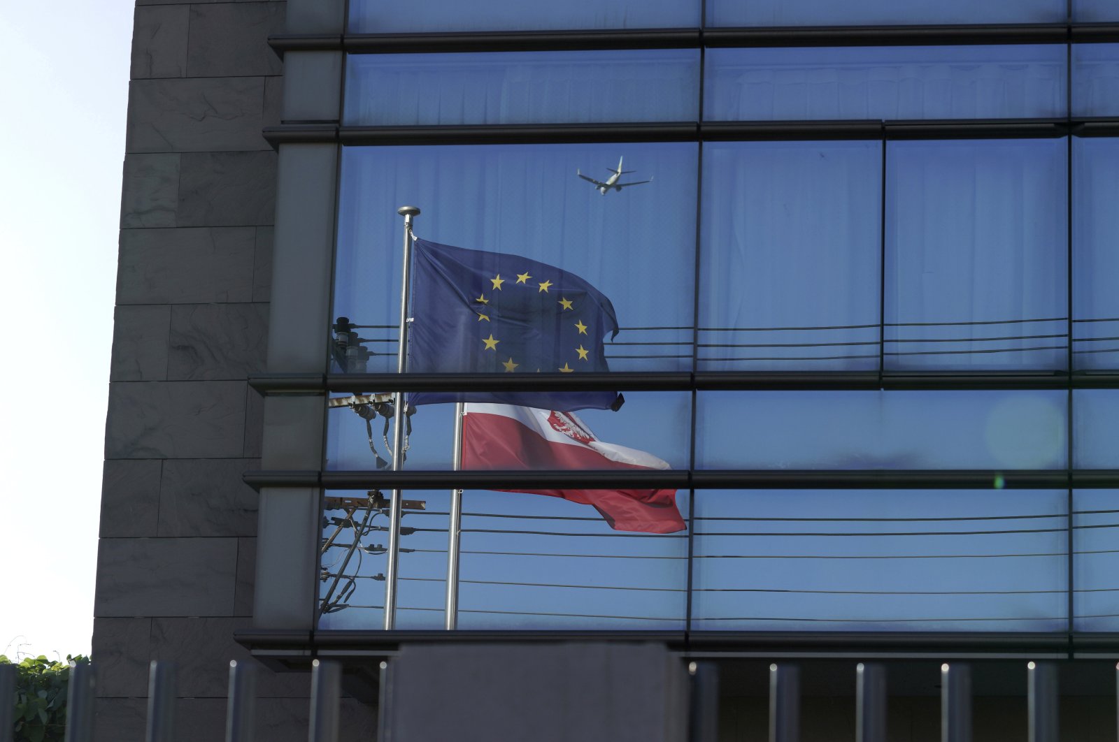 An airplane and flags of Poland and the European Union are reflected on the building of the Embassy of Poland in Tokyo, Aug. 3, 2021. (AP Photo)