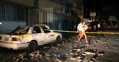A couple walks past a taxi cab that was damaged by falling debris after a strong earthquake in Acapulco, Mexico, Sept. 7, 2021. (AP Photo)