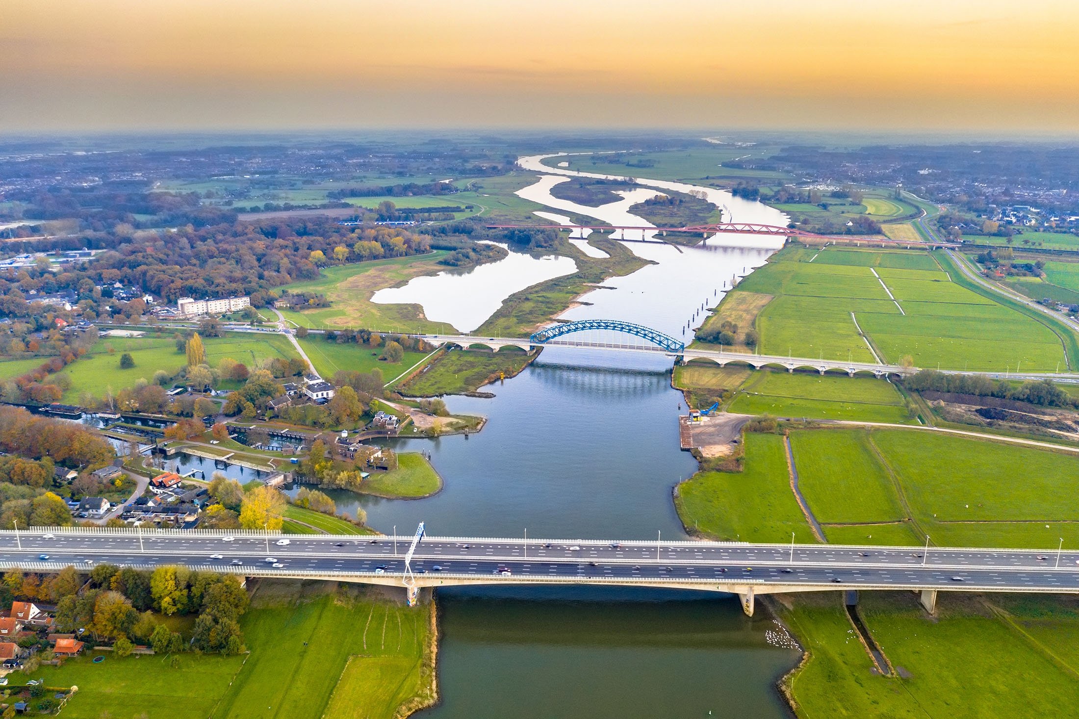 An aerial view of huge lowland river IJssel with highway and railroad bridges through sunset landscape, Zwolle, the Netherlands. (Shutterstock Photo)