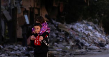 A boy carries a child past damaged buildings at the Yarmouk Palestinian refugee camp on the southern outskirts of Damascus, Syria, Dec. 1, 2020. (Reuters Photo)